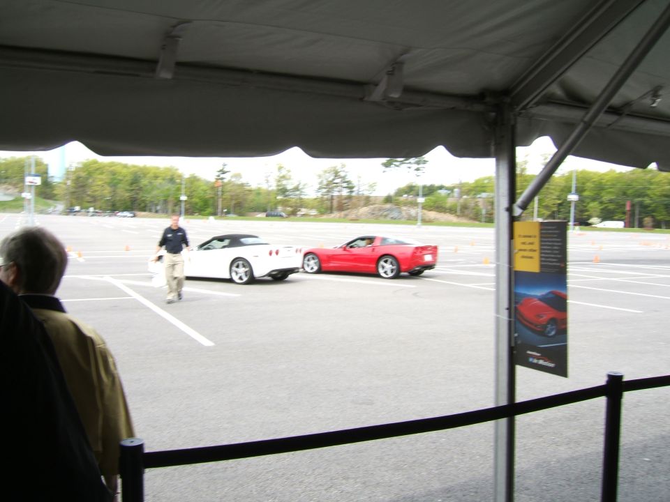 Red and white sports cars on a paved lot with orange cones, a man walks between them