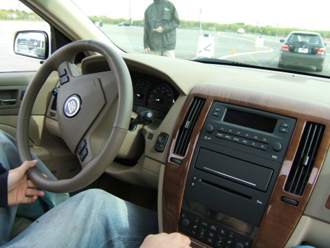 1998 Ford Taurus - Interior view of a car, showing the dashboard, steering wheel with Cadillac emblem, and wood trim. Another car is visible in the background.
