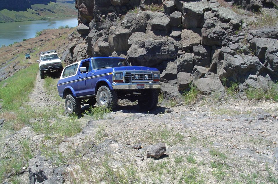 Blue 1978 Ford Bronco on a rocky off-road trail with a river in the background