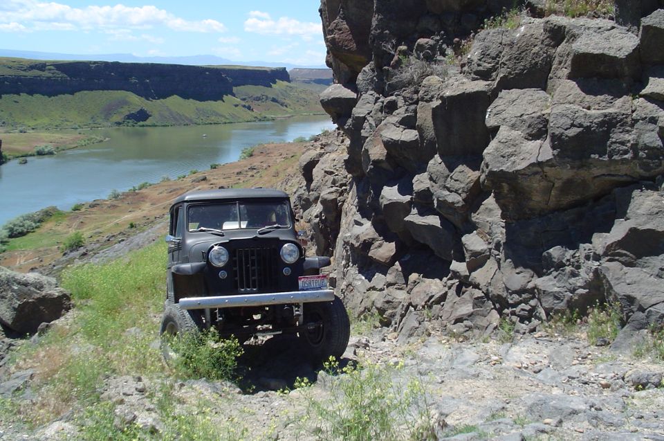 Black 1950s Jeep Willys parked on a rocky trail next to a river