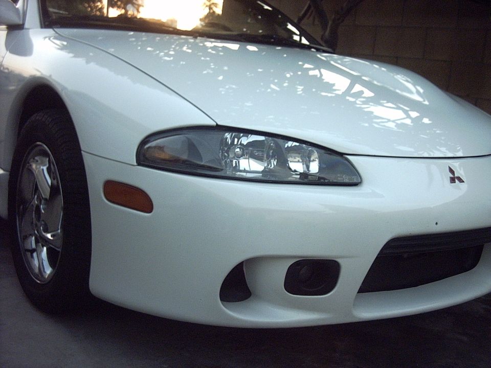 White Mitsubishi Eclipse front three-quarter close-up with headlight and chrome wheel