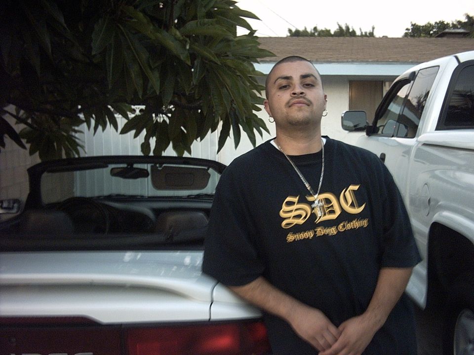 Man in black SDC shirt standing between silver convertible and white pickup in a driveway