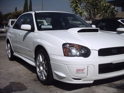 2005 Subaru Impreza - A white 2005 Subaru Impreza WRX STI sedan is shown from the front 3/4 angle, its distinctive hood scoop and STI badging.