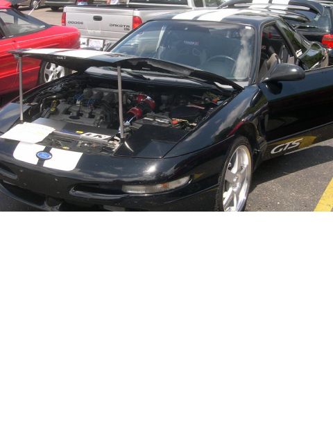 1997 Ford Probe - Black hatchback coupe at an outdoor car show with the hood held open by two chrome prop rods, exposing a V6 with a red cone intake filter a…