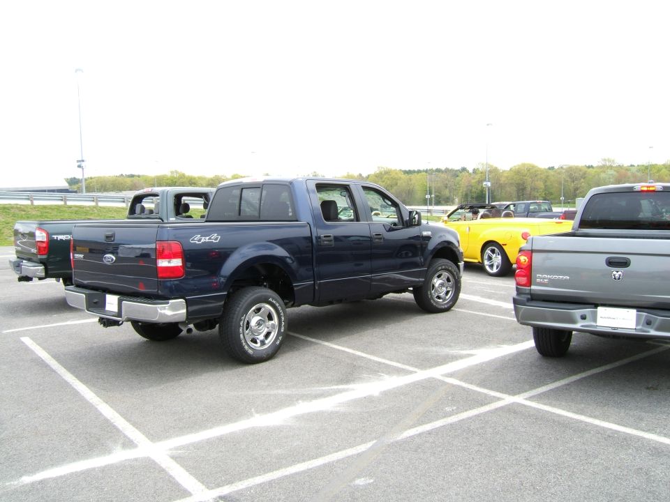 Dark blue Ford F-150 pickup truck parked in a lot, with other trucks and a yellow convertible behind it