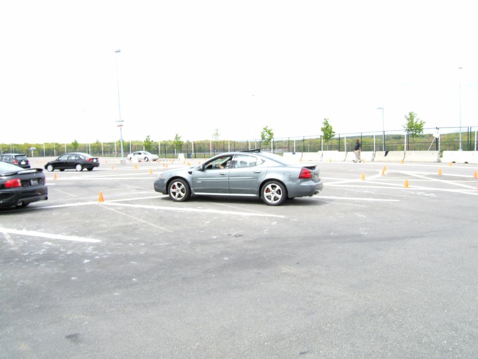 Gray Pontiac Grand Prix driving on a paved lot with orange cones