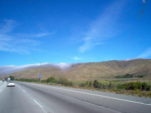 1988 Ford Bronco - A white SUV travels down a highway under a bright blue sky, with rolling hills and a band of fog in the distance.