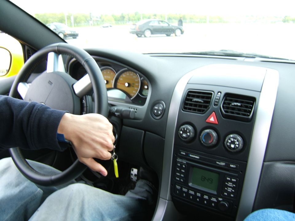 Car interior with hand on steering wheel, dashboard gauges, and radio display showing 8:49