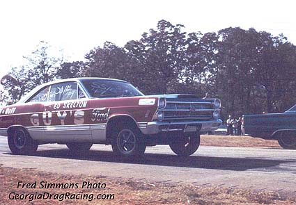 1967 Ford Fairlane - A vintage Ford Fairlane dragster with prominent lettering on its side is captured in motion on a race track.