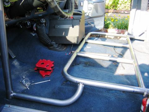 1985 Ford Bronco - The interior of a vehicle shows a partially installed roll cage and blue carpeting.