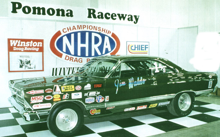 Dark green drag coupe with 'Jim Waldo' lettering and sponsor decals on NHRA display floor