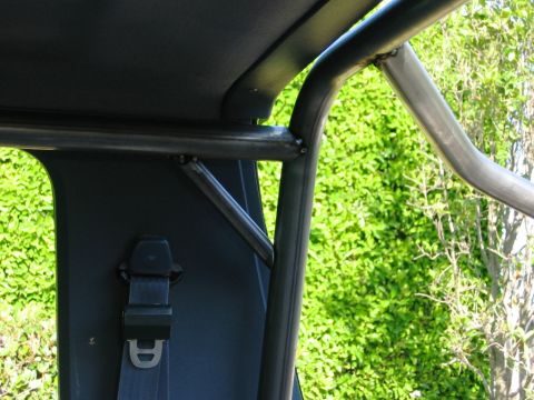 1985 Ford Bronco - Interior view of a vehicle's roll cage and seatbelt, with green foliage visible through the window.