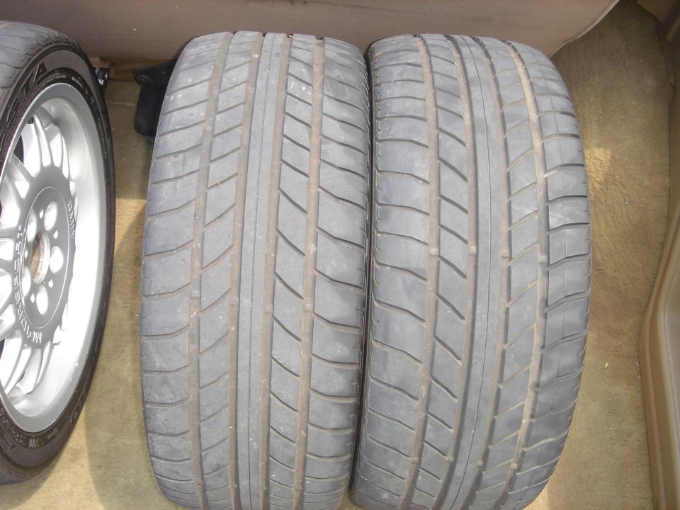 Two directional performance tires standing on tan carpet with a third wheel behind