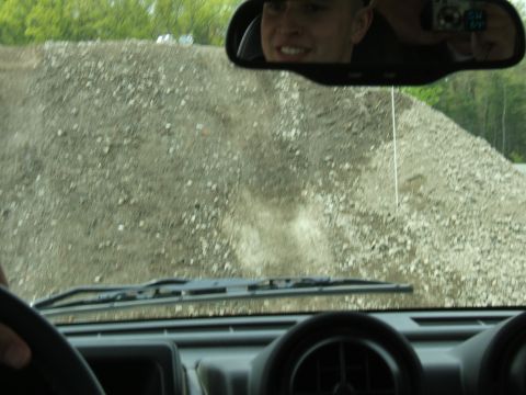1998 Ford Taurus - View from inside a vehicle as it drives on a gravel road, with a person reflected in the rearview mirror.