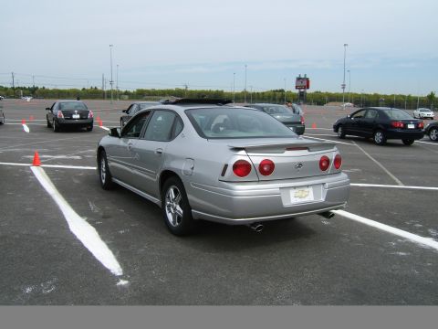 1998 Ford Taurus - Silver sedan parked in a lot with other vehicles and orange cones visible.