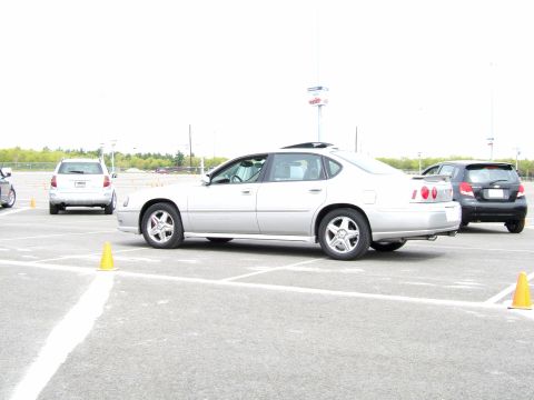 1998 Ford Taurus - A silver sedan is parked in a lot with traffic cones, with other vehicles visible in the background.
