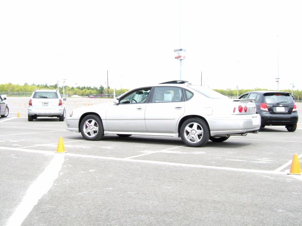 Silver sedan parked in a lot with cones, another car behind it