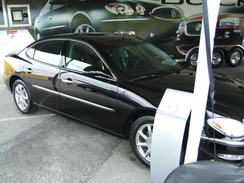 1998 Ford Taurus - A black sedan is displayed at a car show, with other vehicles visible in the backdrop and a watermark at the bottom.