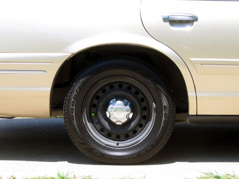 2000 Ford Crown Victoria - Close-up view of the rear wheel and door handle on a gold 2000 Ford Crown Victoria.