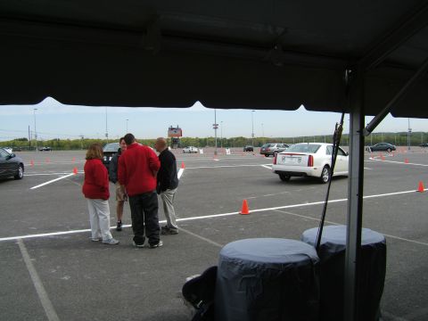 1998 Ford Taurus - A white sedan is viewed from the rear on a paved track, with several people standing nearby and other vehicles in the background.