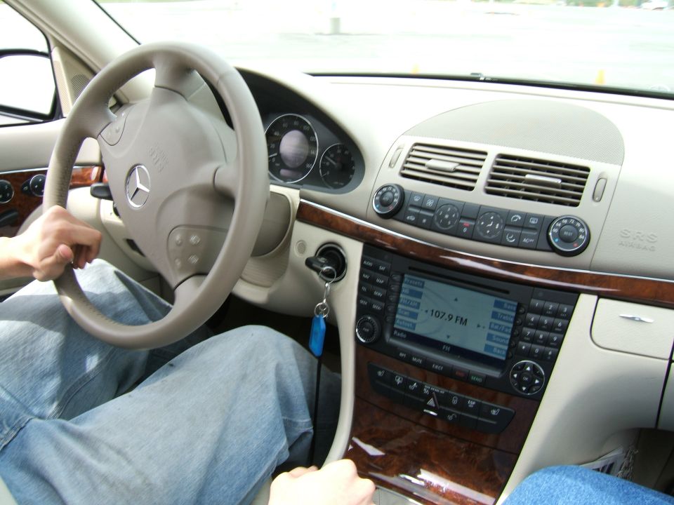 Driver's hands on steering wheel of Mercedes-Benz, showing dashboard and infotainment screen