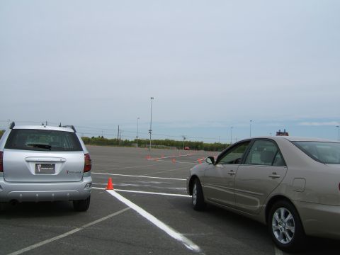 1998 Ford Taurus - Two vehicles, a silver Pontiac Vibe and a tan sedan, are parked in a lot marked with white lines and orange cones.