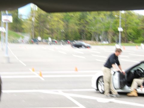 1998 Ford Taurus - Two people are getting into a white sports car on a track with trees in the background.