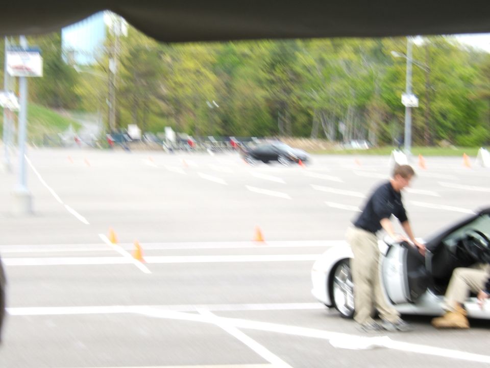 People entering a white sports car on a paved surface with orange cones