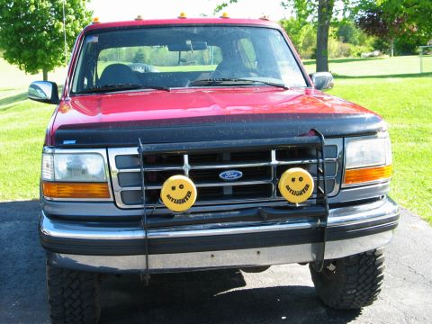 1995 Ford Bronco - This red pickup truck features a brush guard with smiley face fog lights and amber turn signals.