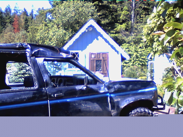 Dark blue two-door 4x4 with roof removed and exposed roll bar, parked by a cottage