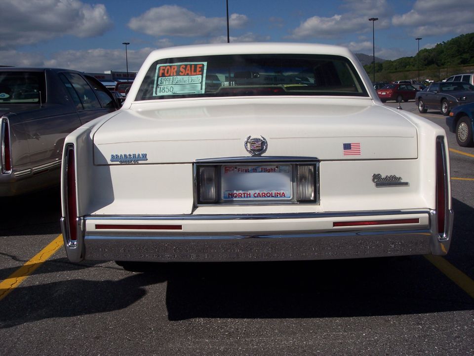 Rear view of a white Cadillac sedan with a $1850 for-sale sign in the rear window, North Carolina plate
