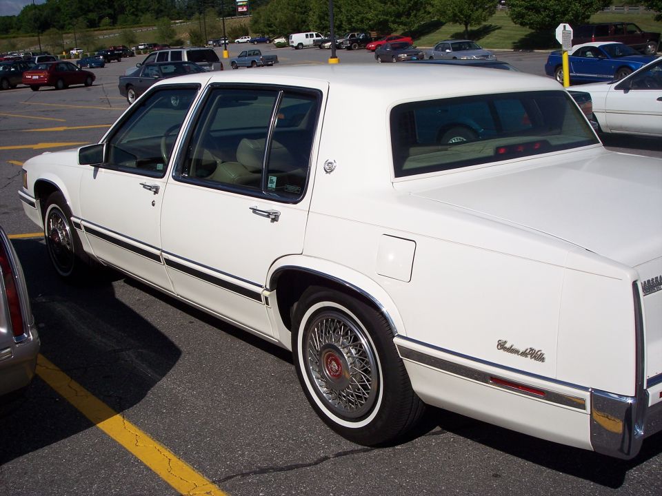 White Cadillac Sedan de Ville sedan, rear left view, wire wheels, in parking lot
