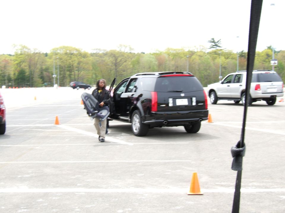 Black Cadillac SRX parked, driver's door open, person carrying bag. White SUV in background