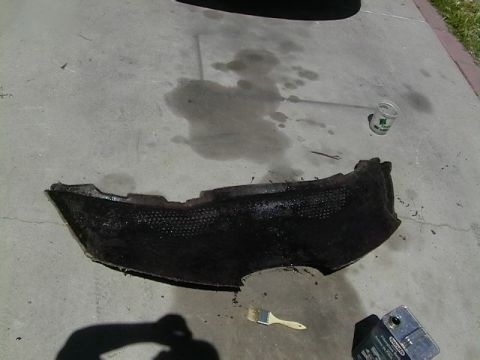 1999 Ford Taurus - A damaged car fender liner lies on the ground next to a brush and some spilled liquid.