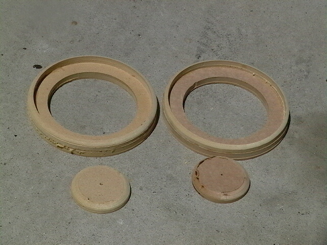 Two wooden speaker mounting rings and two smaller circular pieces on a concrete surface