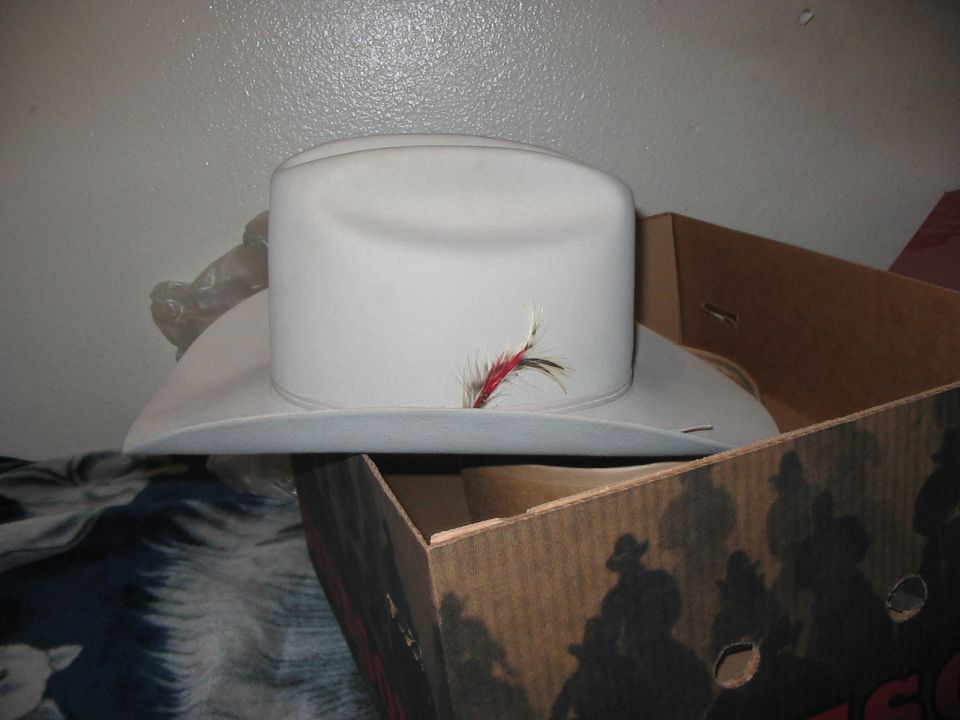 White cowboy hat with a red and brown feather band, resting on a box