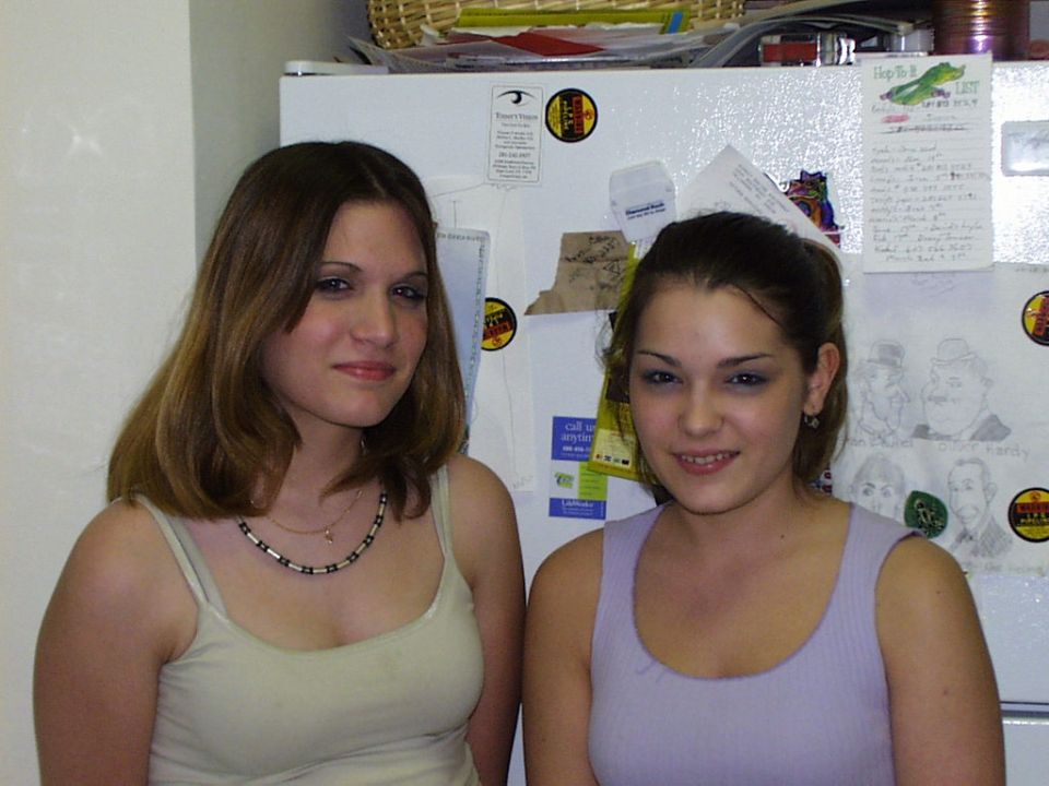 Two young women pose in front of a refrigerator covered in notes and drawings