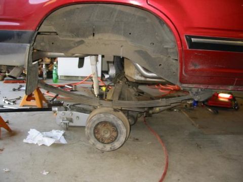 1991 Ford Explorer - The rear suspension and axle of a red vehicle are disassembled for maintenance in a garage setting.