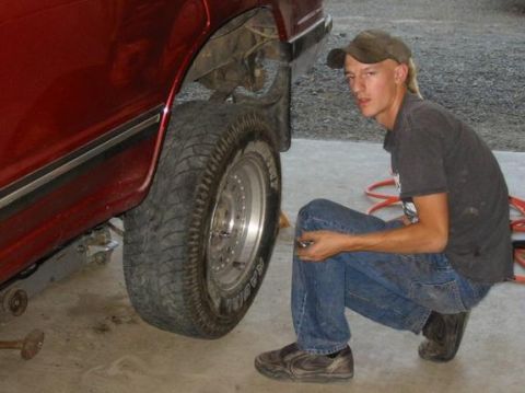 1991 Ford Explorer - Man works on the rear tire of a red 1991 Ford Explorer lifted on a jack.