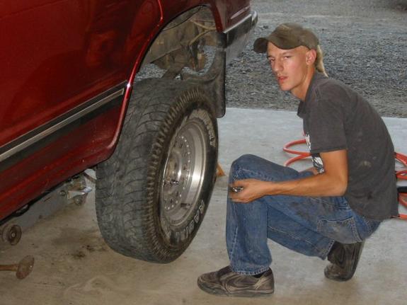 Man crouching beside a red SUV fitting an all-terrain tire on a polished mag wheel