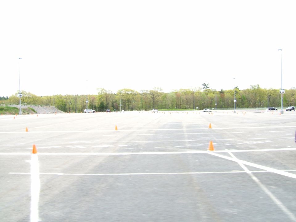 Parking lot with orange cones and several cars in the distance under a bright sky