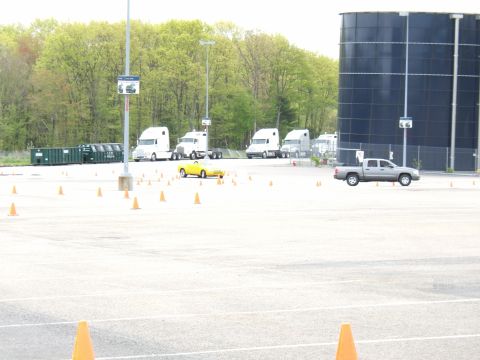 1998 Ford Taurus - A yellow sports car navigates a cone course with semi-trucks in the background.