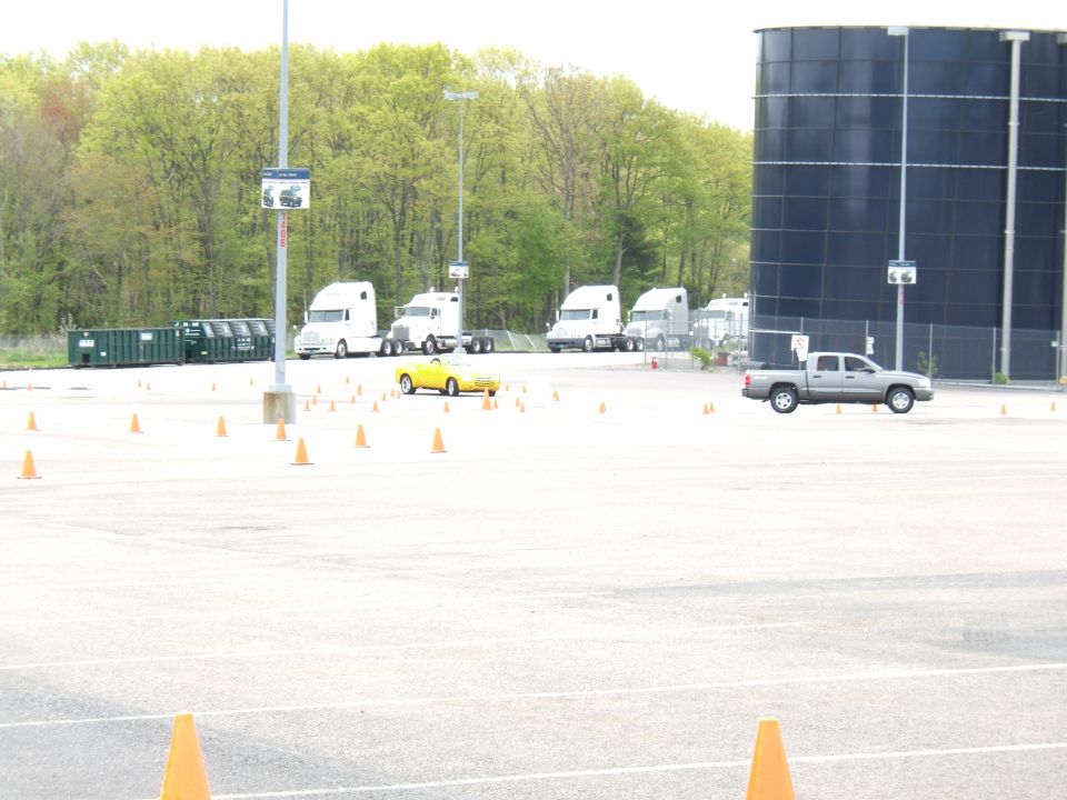 Yellow convertible sports car and several semi-trucks in a parking lot with cones