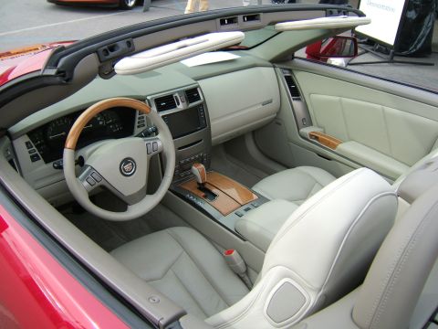 1998 Ford Taurus - Overhead view into the cockpit of a red Cadillac roadster with the retractable hardtop open, showing tan/light-gray leather seats, wood-and…