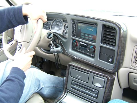 1998 Ford Taurus - Interior of a GMC truck with woodgrain trim and tan dash; a driver grips the GMC-logo wheel beside an aftermarket touchscreen head unit.