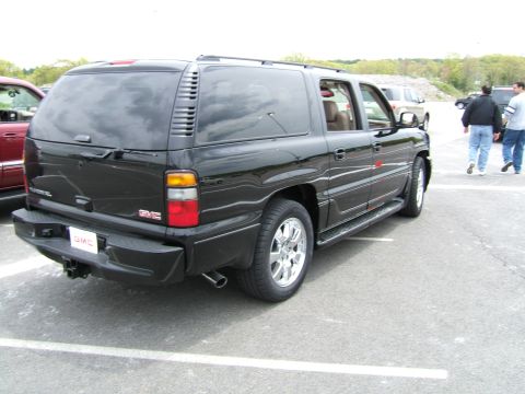 1998 Ford Taurus - Three-quarter rear view of a black GMC Yukon XL Denali full-size SUV parked in a lot, showing the body-color rear bumper with GMC plate, ti…