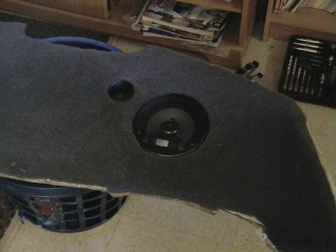 1999 Ford Taurus - A carpeted panel with a speaker cutout and a separate black circular object is seen from above, resting on a laundry basket.
