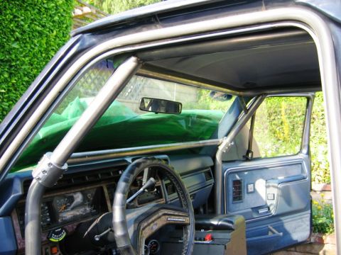 1985 Ford Bronco - The interior of this 1985 Ford Bronco features a custom roll cage and blue upholstery, with a view of the dashboard and door panel.