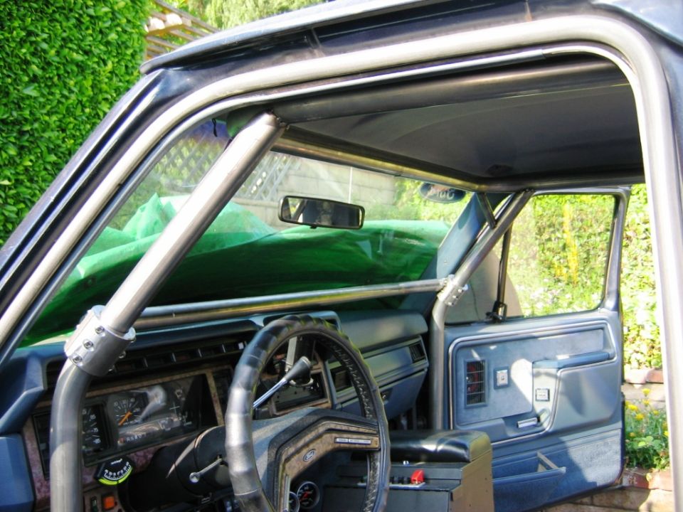 SUV interior with custom bare-metal roll cage along A-pillar and roof, blue trim, steering wheel visible