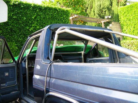 1985 Ford Bronco - Blue Ford Bronco with a custom roll cage, seen from the side with the driver's door open.